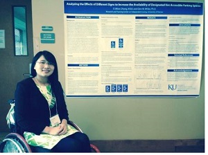 Alice Zhang, a wheelchair user, sitting in a hallway in front of her conference poster about parking accessibility