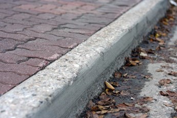 A cement curb borders a brick sidewalk.