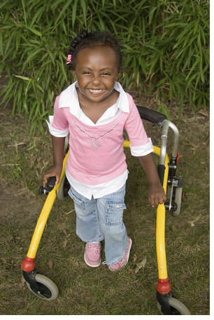 A child using assistive technology to stand upright and smile for the camera